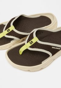 Καφέ σανδάλια τύπου φλιπ-φλοπ με υφή στο καφέ πέλμα, κρεμ εξωτερική σόλα και μαύρο λουράκι από δίχτυ με κίτρινη νέον λεπτομέρεια.