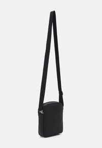 Black crossbody bag with a rectangular shape, made from smooth material. It features a long strap and a zippered compartment. Minimalist design.