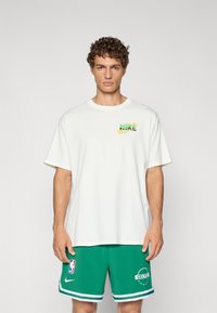 Hvid bomulds t-shirt med et grønt og gult Nike-logo på venstre bryst. Sammen med grønne sports shorts med striber og logo.