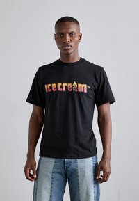 Sort bomulds T-shirt med et farverigt "iskrem" logo og glitrende detaljer. Korte ærmer, rund halsudskæring og afslappet pasform.