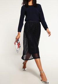 Blusa a maniche lunghe blu navy abbinata a una gonna plissettata in tulle nero. La modella porta una clutch colorata e indossa tacchi con cinghietta argentati.