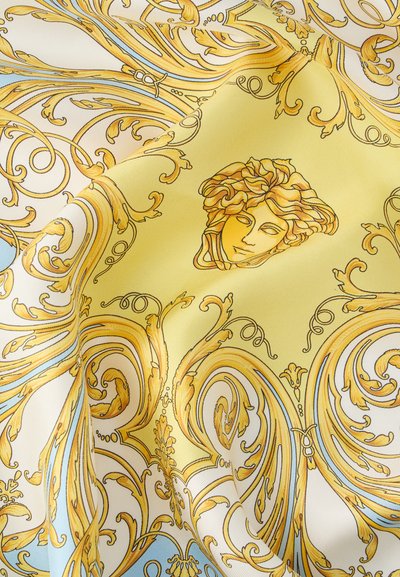 Κίτρινο και μπλε μπαρόκ σχέδιο σε λευκό ύφασμα με περίτεχνες σπείρες και κεντρικό μοτίβο κεφαλής Μέδουσας, διπλωμένο για να δείξει υφή και λεπτομέρεια.