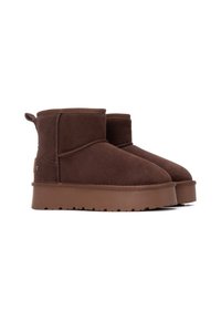 Botas de ante marrón hasta el tobillo con una suela de goma plana, punta redondeada y una pequeña pestaña en la parte trasera. Diseño simple sin patrones o acentos adicionales.