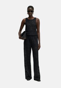 Zwarte gehaakte twee-delige outfit bestaande uit een mouwloos topje en wijde broek, met geometrische patronen en een ontspannen pasvorm.