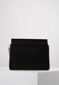 Borsa nera realizzata in materiale liscio, con una patta ripiegata, dettaglio in catena dorata e forma rettangolare con una finitura opaca.