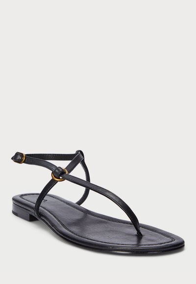 Μαύρο δερμάτινο σανδάλι με λεπτές λωρίδες, επίπεδη σόλα και ένα μικρό χρυσό διακοσμητικό δαχτυλίδι στον αστράγαλο. Μινιμαλιστικός σχεδιασμός και απαλό υλικό.