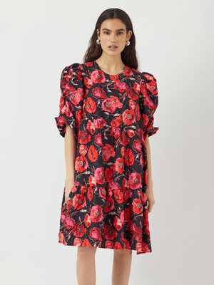 Robe fleurie à manches bouffantes. Tissu noir orné de fleurs de coquelicot rouges et roses. Silhouette en A, longueur genou, avec un col rond.