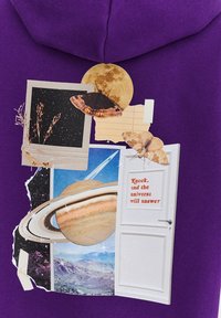 Fialová mikina s koláží nebeských obrázků, včetně měsíce, Saturnu, motýlů a papírových textur. Text: "Zaklep, a vesmír odpoví."