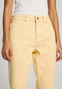 Jeans de mezclilla amarillos con un diseño de pierna recta. Presentan bolsillos frontales, un cierre de botón y una textura sutil. Sin patrones ni adornos visibles.
