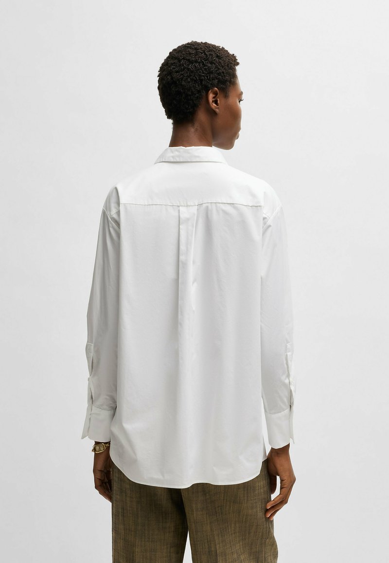 Camisa blanca de manga larga con cuello, que presenta un diseño de espalda recta y puños abotonados. Fabricada en tejido suave y ligero.