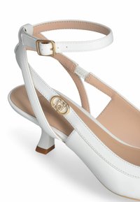 Valge nahkne slingback king, millel on madal konts ja kuldse tooni pandlaaktsent. Omab minimalistlikku disaini ja sileda tekstuuri pealmises osas.