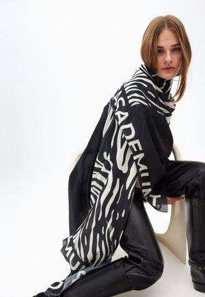 Schwarz-weiß gestreifter Schal im Zebra-Stil mit auffälligen Textakzenten, aus leichtem Stoff, über die Schultern drapiert über einem schwarzen Outfit.