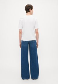 Witte korte mouw t-shirt gecombineerd met wijde blauwe spijkerbroek, met een klassieke pasvorm en zichtbare stiksels op de zakken.