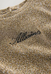 Särav kuldne kangas peene tekstuuriga; musta käekirjaga "Allsaints" logo. Ümmargune kaelus kerge sära jaotusega.