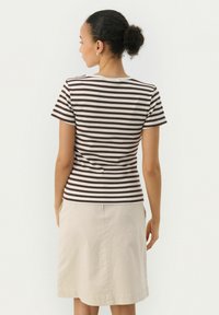 T-shirt rayé marron et crème avec une texture côtelée, à manches courtes et un col rond, associé à une jupe beige jusqu'aux genoux.