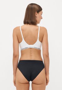 Witte bralette met verstelbare banden en logo-detail; gecombineerd met een hoge taille zwarte slip. Gladde stof, aansluitend ontwerp.