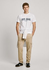 Biela bavlnená tričko s logom "PEPE JEANS", béžové cargo nohavice s vreckami a čierne tenisky. Neformálny outfit, minimalistický dizajn.