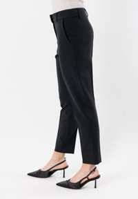 Pantaloni neri su misura con vestibilità slim, caratterizzati da una vita media, tasche laterali e una texture liscia. Abbinati a décolleté nere con punta a slingback.