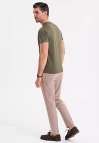 Camiseta ajustada de color verde oliva, de mangas cortas y cuello redondo; combinada con chinos ligeros de color beige y mocasines marrones, diseño minimalista.
