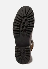 Suela de bota marrón con un rugoso revestimiento de goma negra, que presenta profundos surcos y patrones en forma de estrella para ofrecer tracción y estabilidad. Material duradero.