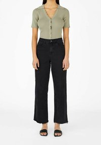 Groene geribbelde top met korte mouwen en V-hals, met knoopsluiting; gecombineerd met hoge zwarte wijde jeans met rafelige zomen.