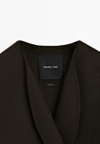 Ciemnobrązowy wełniany płaszcz z szerokim kołnierzem i metką z napisem "Massimo Dutti". Miękka tekstura i minimalistyczny design.