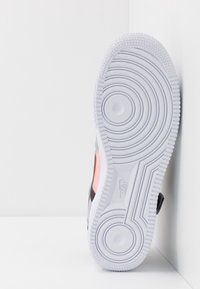 Vit sneakersula med texturerade cirkulära spår, med en slät grå yta och en piff av rosa på sidan, intill en platt bakgrund.