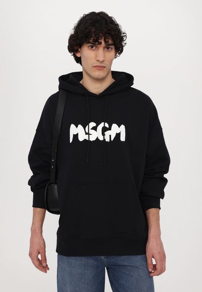 Felpa nera con logo bianco "MSGM", cordini e tasca frontale. Abbinata a jeans azzurri e una piccola borsa nera. Design casual.