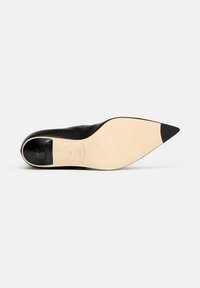 Zapato de tacón alto de cuero negro con punta afilada y suela beige. Presenta una textura suave y un sutil detalle de costura cerca del tacón.
