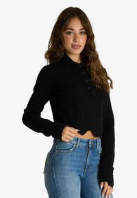 Maglione corto nero con finitura testurizzata, colletto, quattro bottoni e maniche lunghe. Indossato con jeans a vita alta di colore azzurro chiaro.