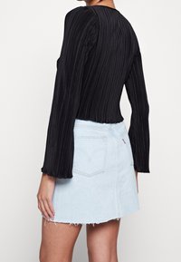 Haut noir à manches longues plissé associé à une mini-jupe en denim bleu clair avec ourlet effiloché et poches arrière.