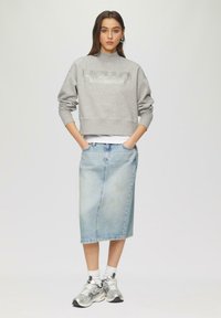 Grijze cropped sweatshirt met de tekst "HELLO", gecombineerd met een lichte spijkerrok tot de knie. Witte sokken en zilveren sneakers maken de look compleet.