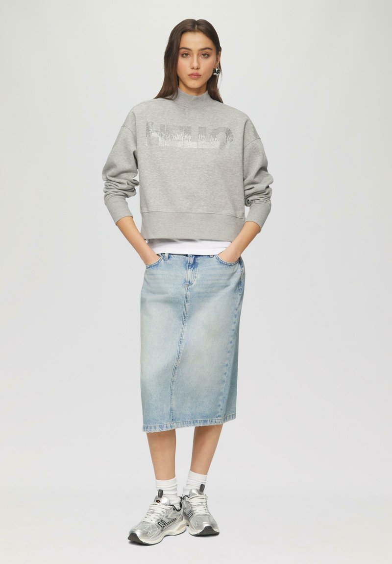Grijze cropped sweatshirt met de tekst "HELLO", gecombineerd met een lichte spijkerrok tot de knie. Witte sokken en zilveren sneakers maken de look compleet.