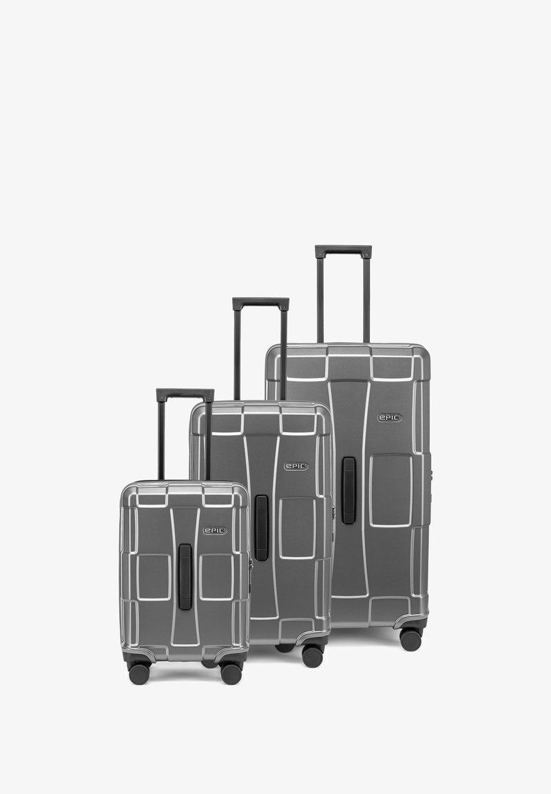 Trois valises rigides grises de petites, moyennes et grandes tailles avec des poignées extensibles et quatre roulettes pivotantes chacune.