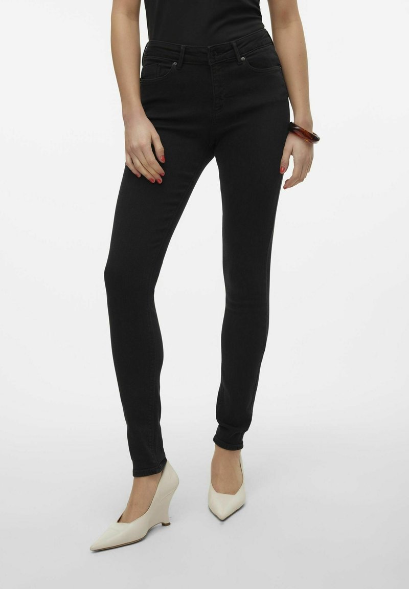 Jeans ajustados negros de mezclilla con una cintura alta, que presentan una textura suave, combinados con unos tacones de punta color crema.