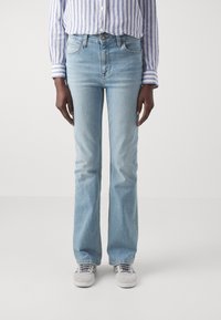 Lichtblauwe flared jeans van denim, met vijf zakken en een subtiele vervaging. Gecombineerd met grijze sneakers en een gestreept shirt.