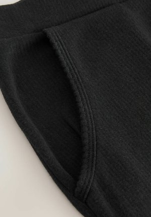 Schwarzer Baumwollstoff mit weicher Textur, ausgestattet mit einer Seitentasche und einem gerippten Bund. Das Design ist schlicht und hat keine sichtbaren Muster.