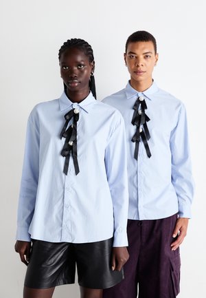 Light blue button-up shirts with black ribbon accents and faux pearls down the front. One model wears leather shorts, the other, purple cargo shorts.