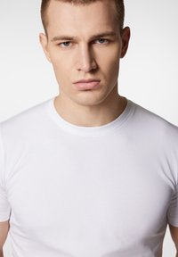 Biała koszulka z okrągłym dekoltem, wykonana z gładkiego, lekkiego materiału. Dopasowany krój z krótkimi rękawami, bez widocznych wzorów czy akcentów.