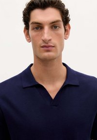 Marineblå pullover med v-hals og korte ærmer. Lavet af et blødt, strikket materiale. Har en klassisk krave og minimal dekoration.