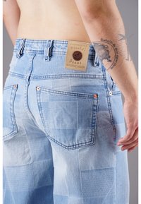 Helle blaue Jeans aus Denim mit einem Patchwork-Design. Zu den Merkmalen gehören kupferfarbene Beschläge und ein gebrandeter Lederriegel am Bund.