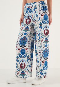 Witte gestreepte broek met blauwe, rode en teal bloemenprints. Comfortabele pasvorm met een elastische tailleband en zijzakken, gedragen met witte sneakers.