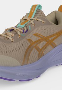 Μπεζ και πορτοκαλί παπούτσι τρεξίματος Asics με μωβ και ανοιχτό μπλε σόλα, κορδόνια με σχέδιο και λεπτομέρειες από δίχτυ στο πάνω μέρος.