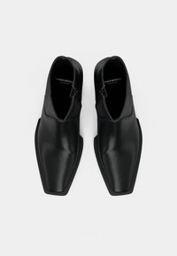 Bottines en cuir noir avec une texture lisse, un bout pointu et des fermetures éclair sur les côtés. Présente un design minimaliste avec une finition mate.