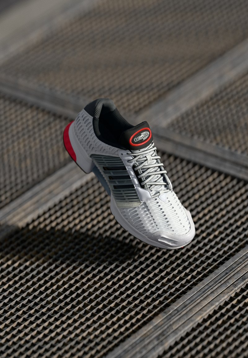 Lichtgewicht sportieve schoen in grijs met een gestructureerde bovenkant, rode accenten en een zwarte kraag. Beschikt over een geperforeerd ontwerp voor ademend vermogen.