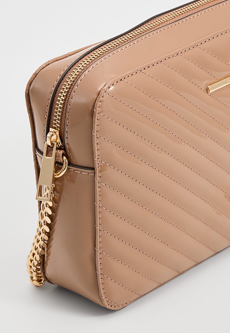 Sac à main en cuir verni tan avec un design matelassé, des accessoires en or et une fermeture éclair. La chaîne sur le côté ajoute un détail. Forme rectangulaire.