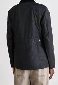 Černá bunda vyrobená z texturované tkaniny, s manžetou z kordu, s patentkami v pase a s označením značky vzadu.