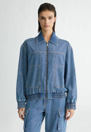 Giacca di jeans con base blu, motivo a pois bianchi, chiusura frontale con zip, colletto a camicia e polsini e orlo elasticizzati.