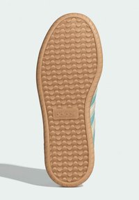 Adidas shoe outsole in beige rubber with a textured grip pattern; side features three light blue stripes against a white background.