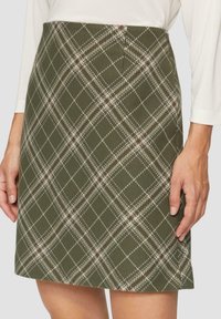 Spódnica w kratę w kolorze oliwkowej zieleni z teksturowanym wykończeniem; posiada białe i bordowe linie tworzące wzór diamentowy; długość do kolan.